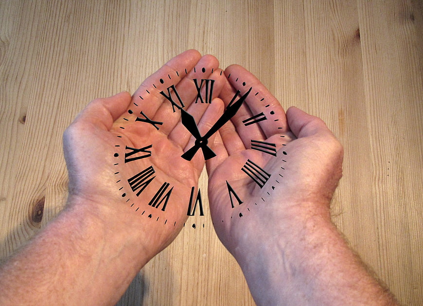 Hands holding clock face on wooden background