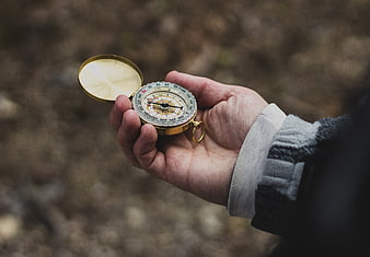 Hand holding vintage brass compass in outdoor nature setting