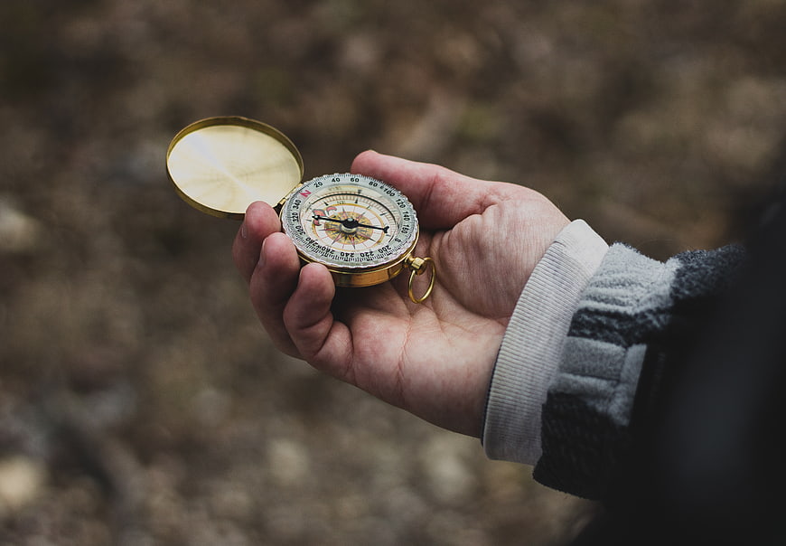 Hand holding vintage brass compass in outdoor nature setting