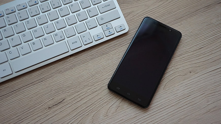 Black Smartphone and White Keyboard on Wooden Desk