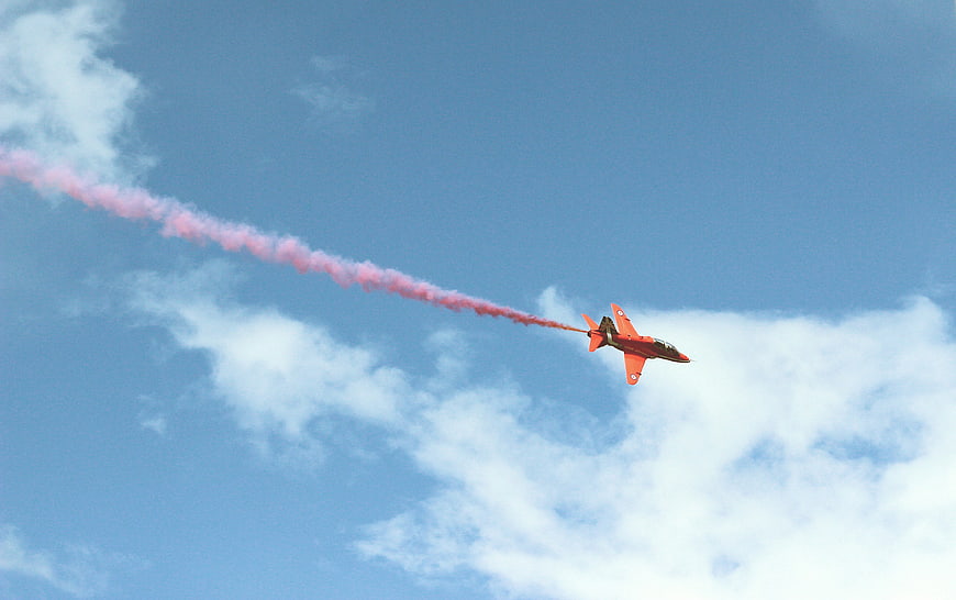 Red Jet Plane with Pink Smoke Trail in Blue Sky
