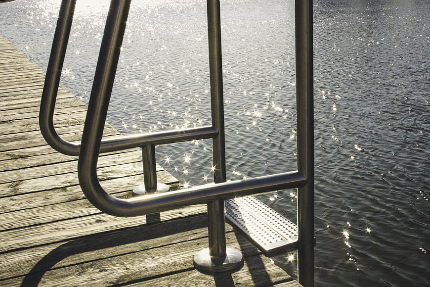 Stainless steel ladder on wooden dock with sparkling water