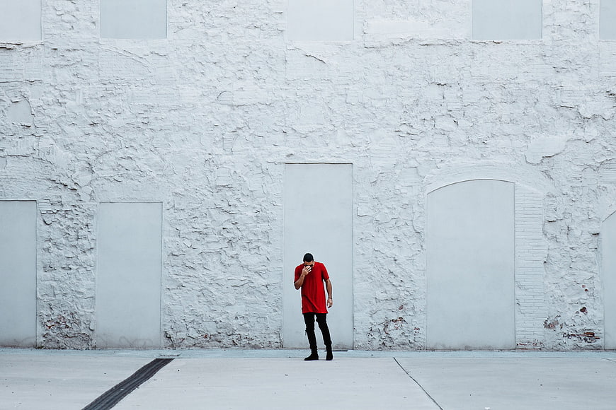 Man in Red Shirt Standing Against White Brick Wall