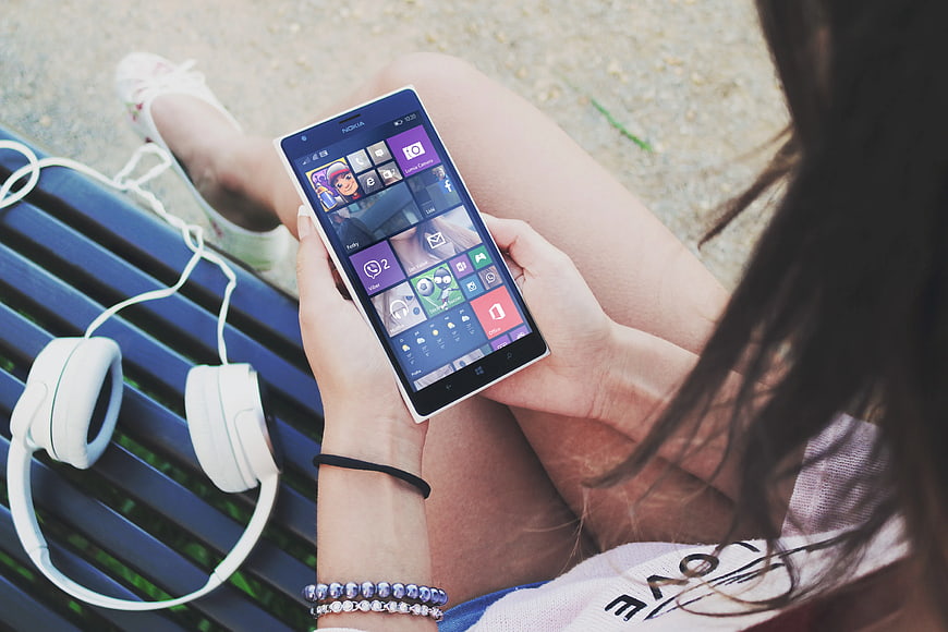 Woman holding smartphone with headphones on blue bench