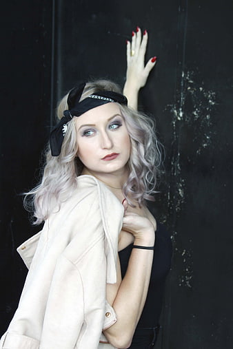 Stylish blonde woman with headband posing against black wall