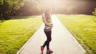 Pregnant woman walking in park holding belly