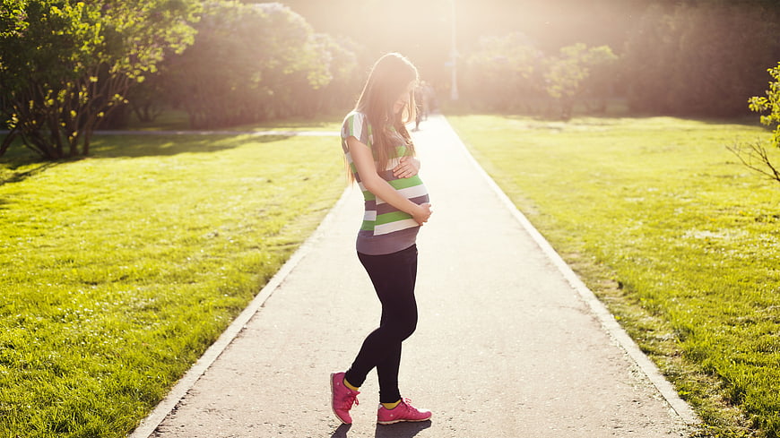 Pregnant woman walking in park holding belly