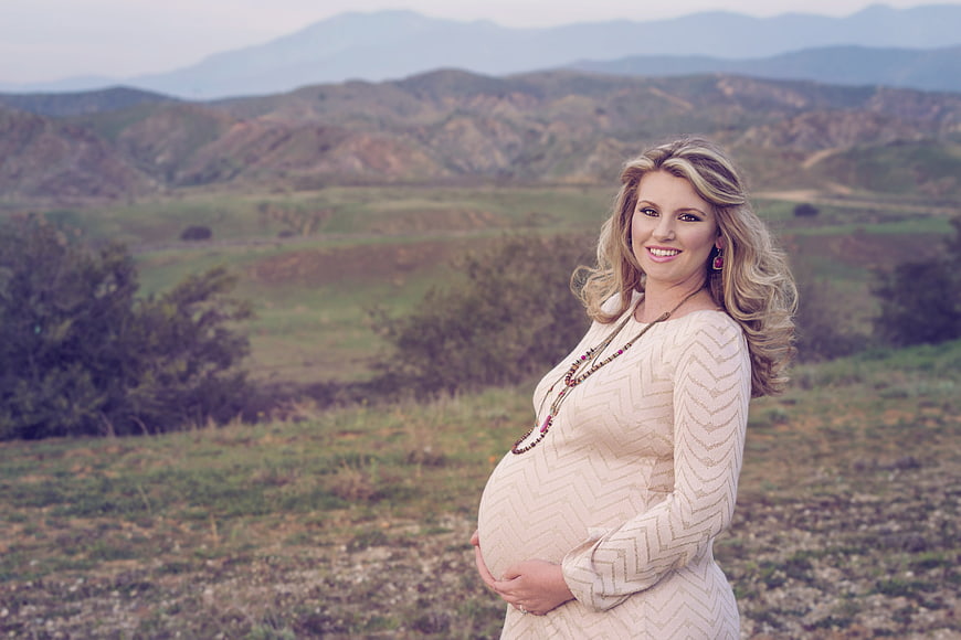 Pregnant woman portrait in beige dress with mountain landscape background