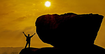 Silhouette of Man with Arms Raised on Rock at Sunset