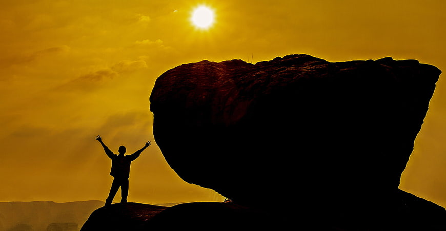 Silhouette of Man with Arms Raised on Rock at Sunset