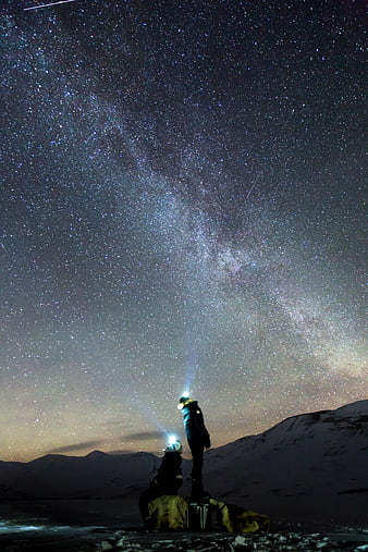 Two explorers with headlamps under the Milky Way in snowy mountains