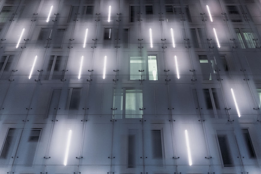 Modern glass building facade with vertical lights at night
