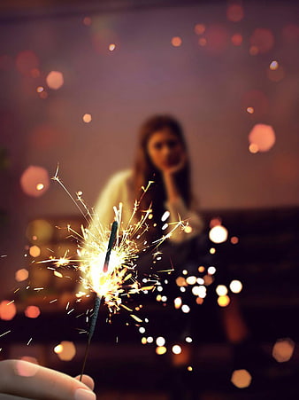 Sparkler in hand with blurred woman and bokeh lights at night
