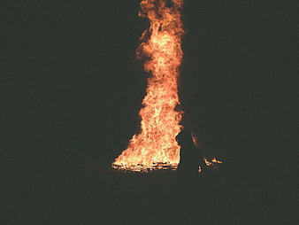 Silhouette of Woman Sitting by Large Bonfire at Night
