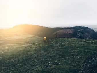 Hikers on grassy hill ridge at sunrise with sun flare