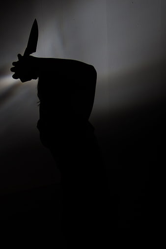 Silhouette of person holding knife in dark room