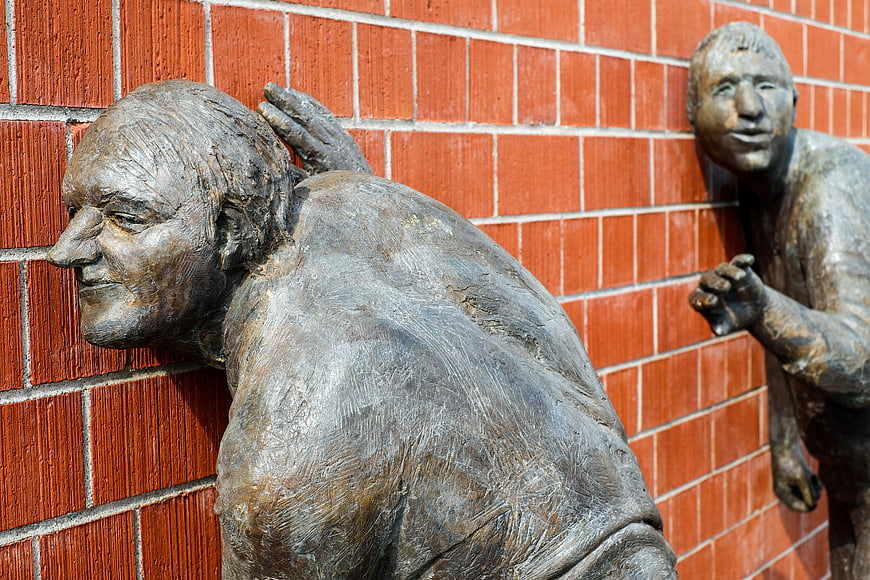 Bronze Sculptures of Men Listening Against Red Brick Wall