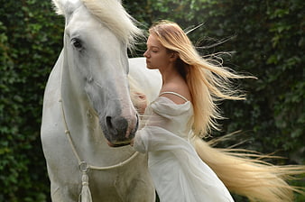 Blonde Woman in White Dress Embracing White Horse in Green Garden