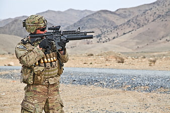 Soldier in camouflage uniform aiming rifle in arid mountainous terrain