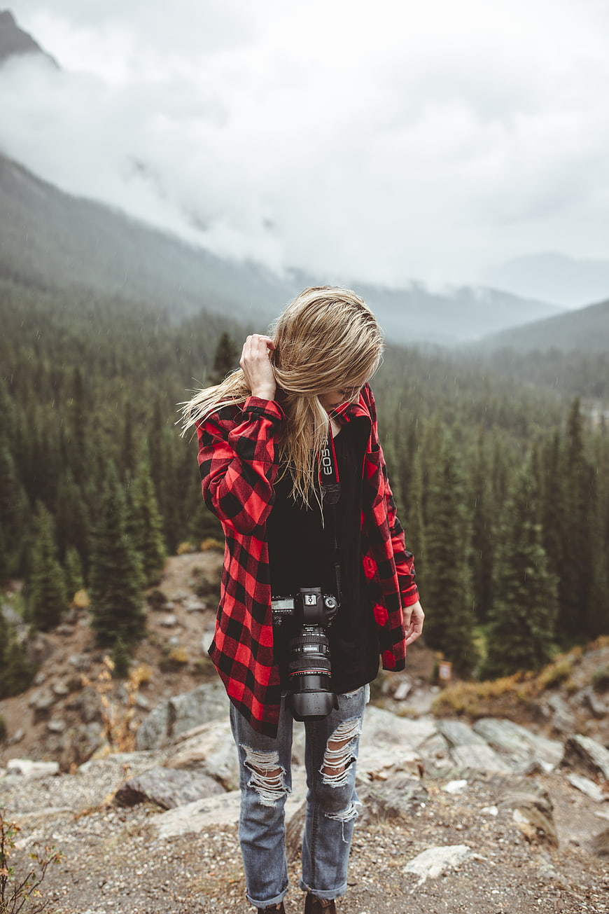 Female photographer with camera in red flannel shirt on mountain trail