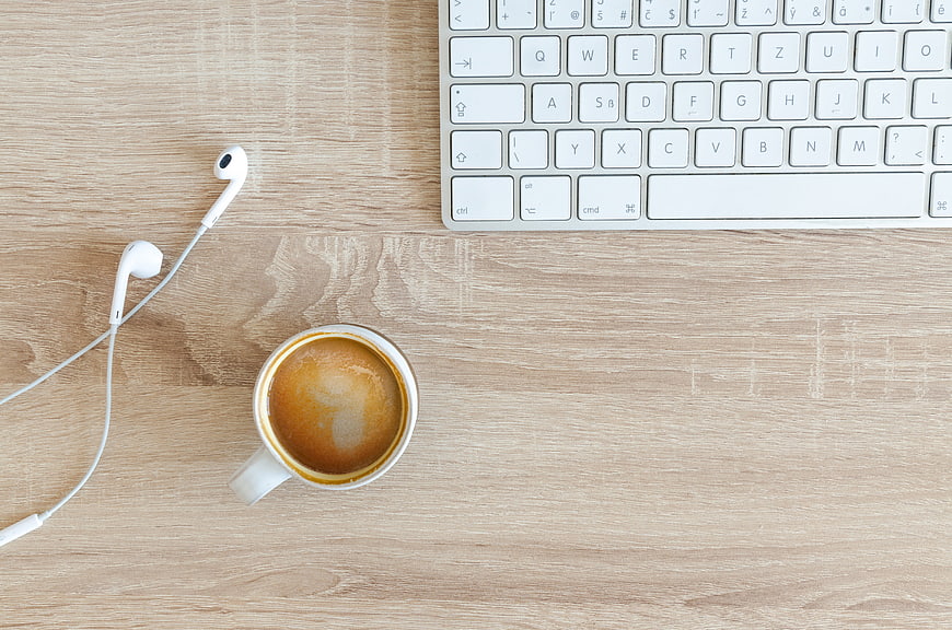 Top View of Coffee, Earphones, and Keyboard on Wooden Desk