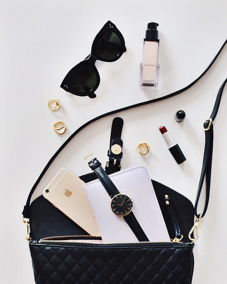 Flat lay of black handbag with accessories and makeup
