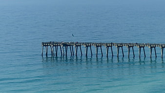 Long wooden pier extending into calm blue ocean water