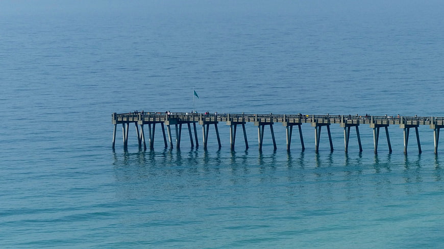Long wooden pier extending into calm blue ocean water
