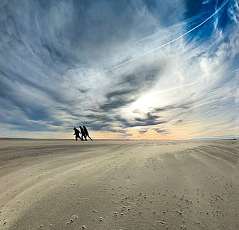 Three people walking on sandy beach under dramatic sky