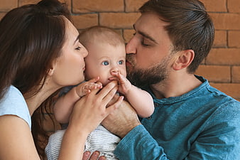 Young parents kissing baby cheeks against brick wall