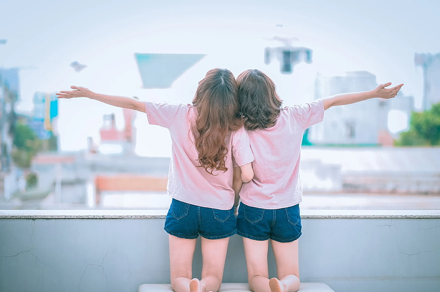Two Girls Kneeling on Balcony Watching Drone