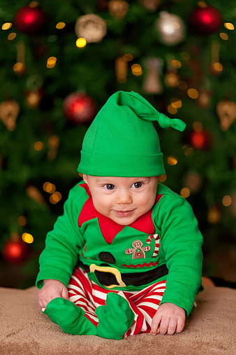 Cute Baby in Elf Costume Sitting in Front of Christmas Tree