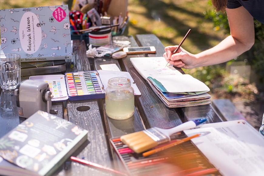 Woman painting watercolors outdoors on a wooden table