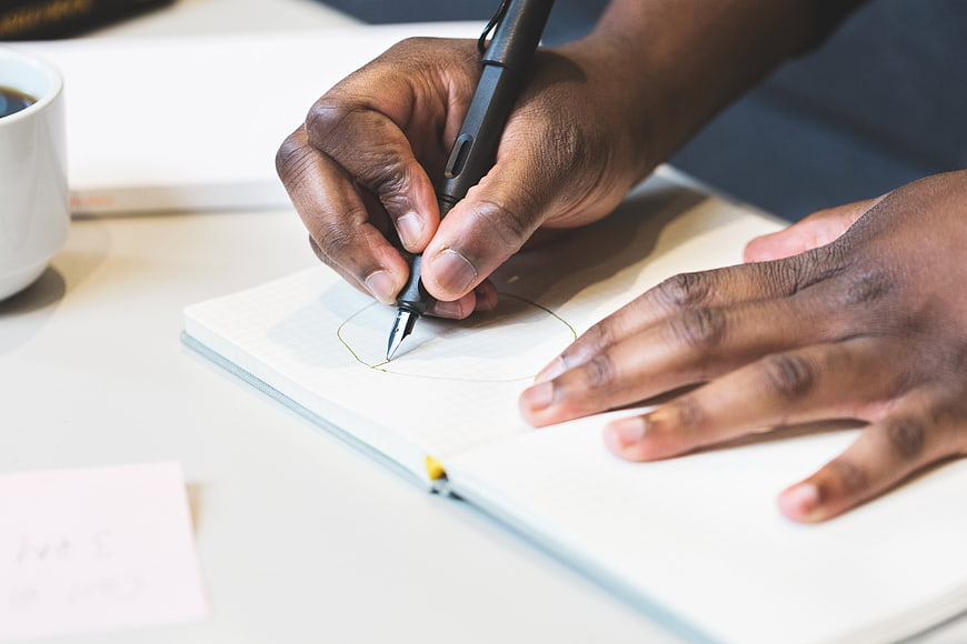 Close-up of hands sketching in a notebook with a pen