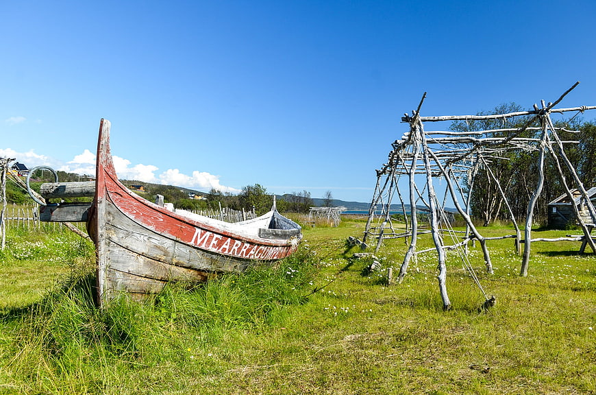 Traditional wooden boat and fish drying racks in green field