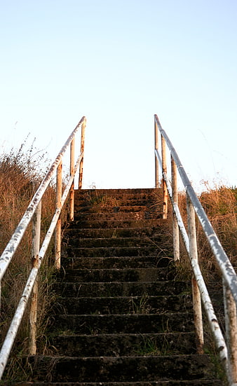 Rusty metal stairs leading up a grassy hill against blue sky