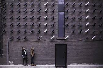 Two women standing under rows of security cameras on gray wall