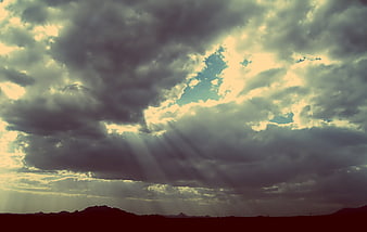 Dramatic sunbeams breaking through dark storm clouds over desert landscape