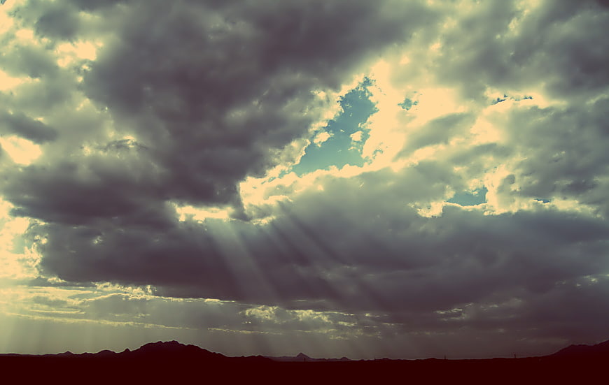 Dramatic sunbeams breaking through dark storm clouds over desert landscape