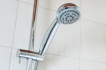 Chrome shower head spraying water on white tiled wall