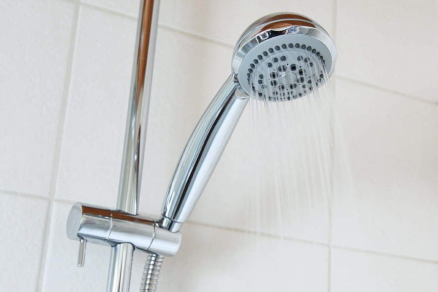 Chrome shower head spraying water on white tiled wall