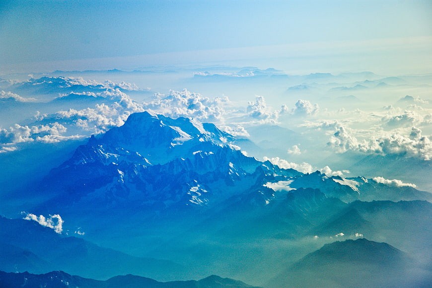 Snow-capped mountain peak rising above clouds in blue landscape