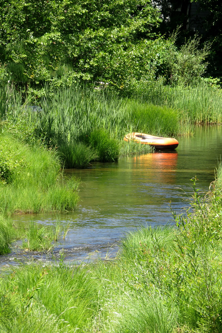 Orange rubber boat moored in a lush green river stream