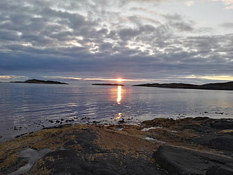 Sunset over rocky Norwegian coastline with algae-covered stones