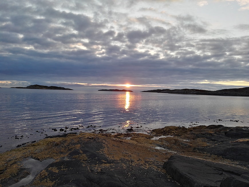 Sunset over rocky Norwegian coastline with algae-covered stones