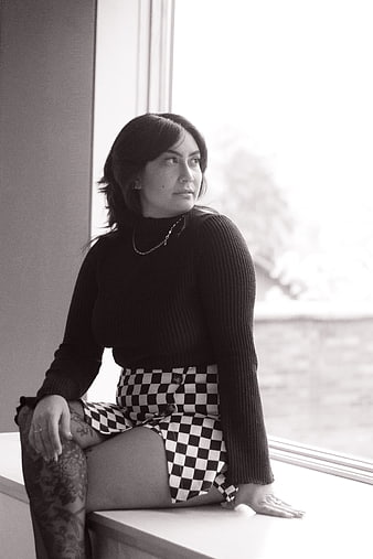 Woman in Checkered Skirt Sitting by Window in Black and White