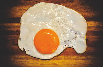 Fried egg with bright orange yolk on rustic wooden surface