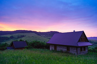 Rustic wooden cabins on a green hillside at sunset