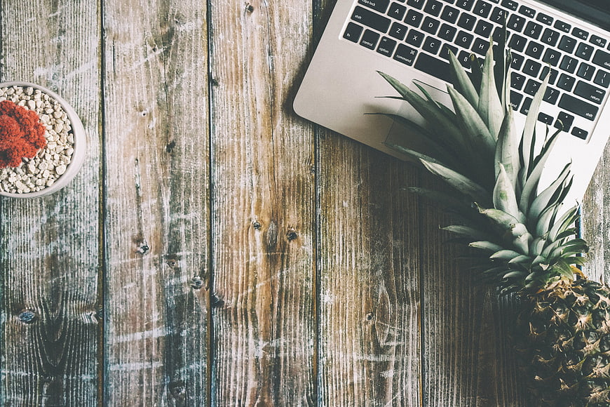 Flat lay of pineapple, laptop, and cactus on rustic wooden desk