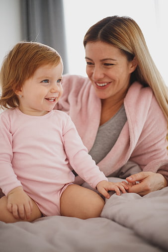 Happy Mother and Toddler Daughter Laughing Together in Bed